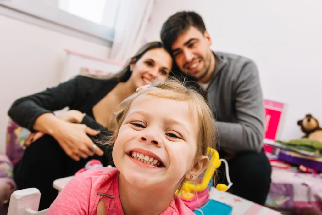A smiling young girl with her parents in the background, representing a positive pediatric dental experience in Fairfield